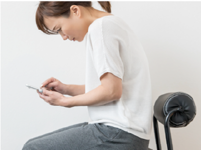 スマートフォンを見ながら前傾姿勢になり、猫背になっている女性
