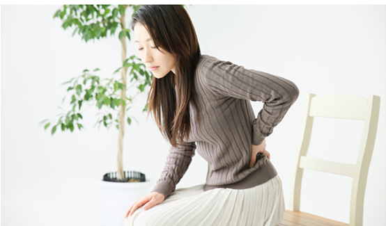 椅子に座って腰に手を当て、腰痛に悩む女性