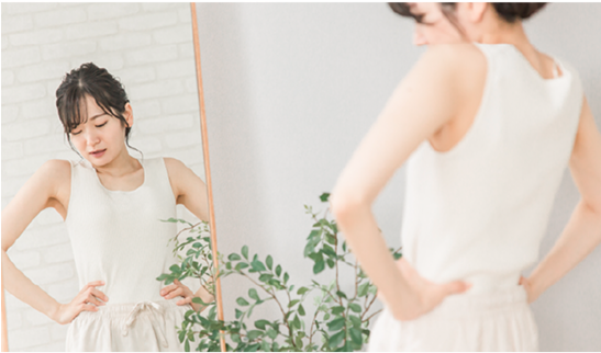 鏡の前で腰に手を当て、体型の変化を気にする女性