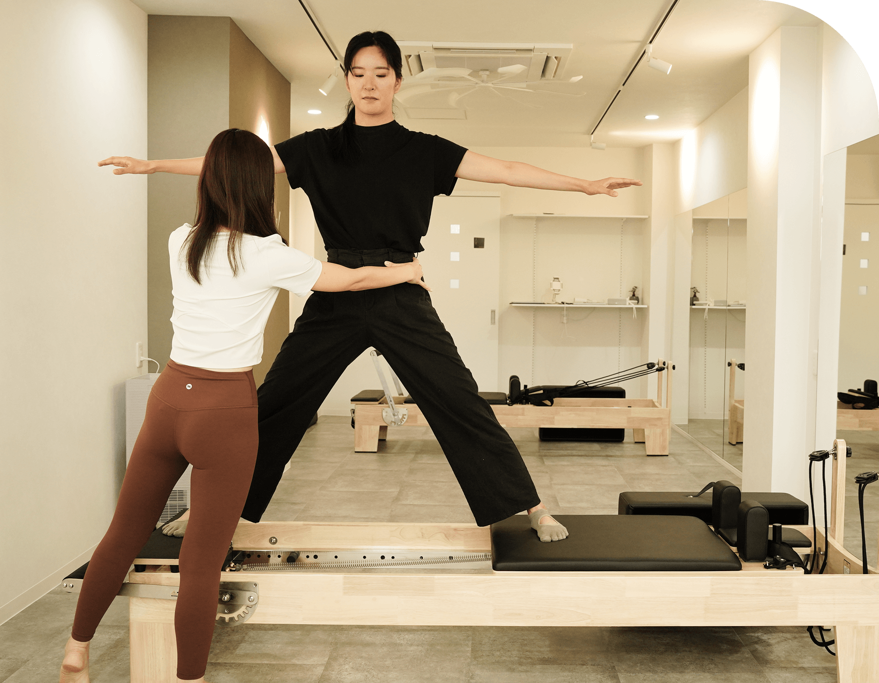 ピラティスマシンで姿勢を整えるトレーニングを行う女性と指導するトレーナー