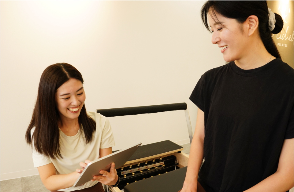 タブレットを使って説明をするピラティスインストラクターと笑顔で話す女性