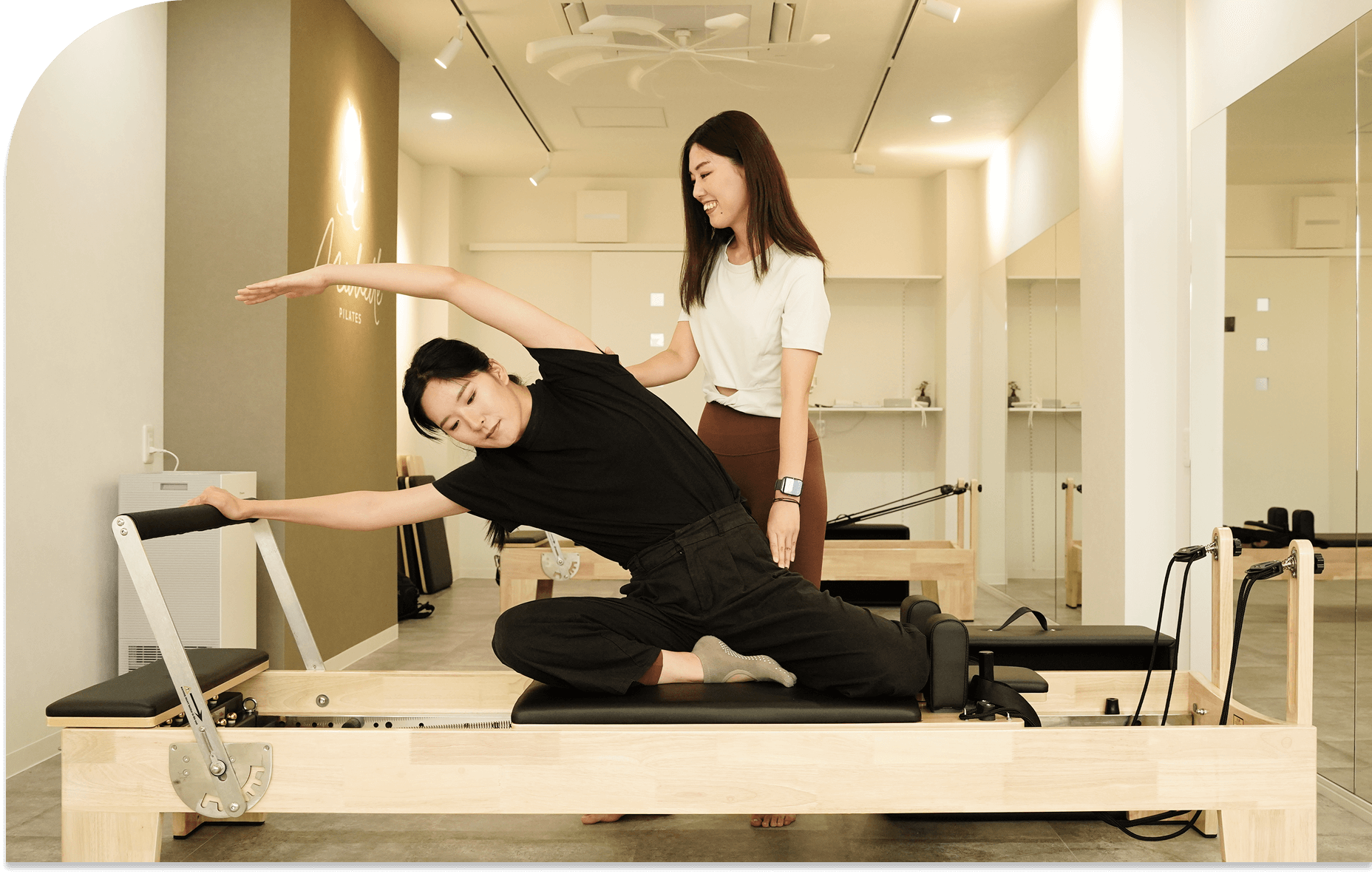 ピラティスマシンでストレッチをする女性と、それをサポートするインストラクター